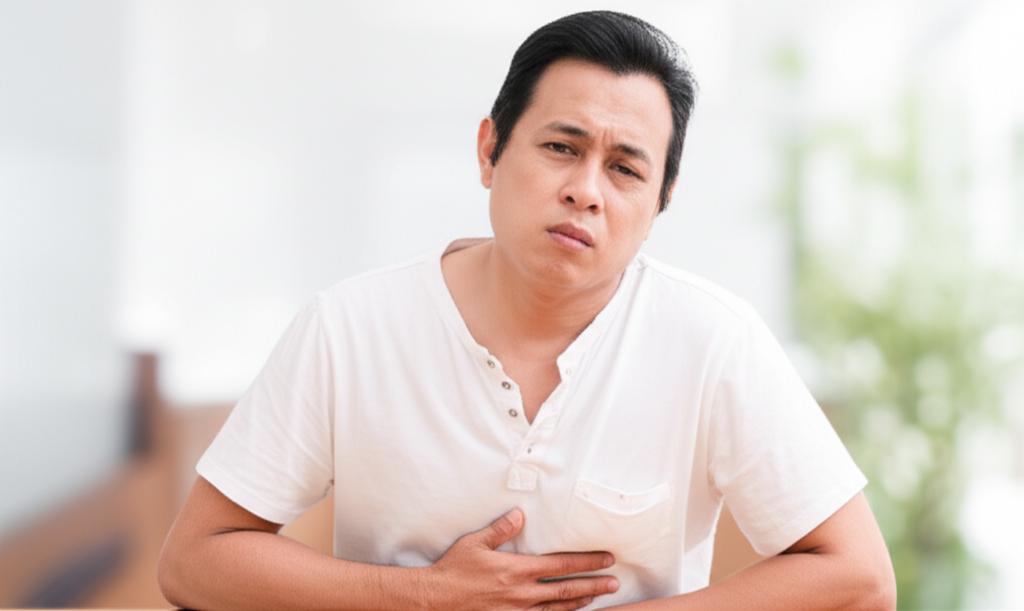 Prompt: A middle-aged Malaysian man looking slightly uncomfortable while sitting at a desk, subtly touching his lower abdomen, soft focus background.