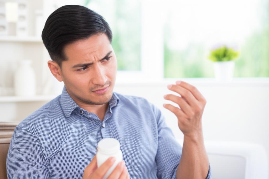 A man looking thoughtful and slightly concerned, perhaps holding a pill bottle, in a calm, health-focused setting. Soft lighting.