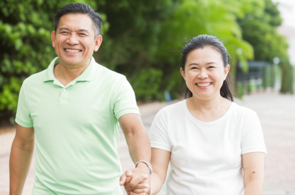 A smiling middle-aged Malaysian couple holding hands, looking happy and energetic outdoors