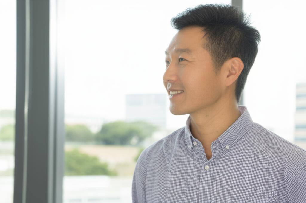 A confident and energetic middle-aged Asian man smiling and looking out a window in a modern office setting.